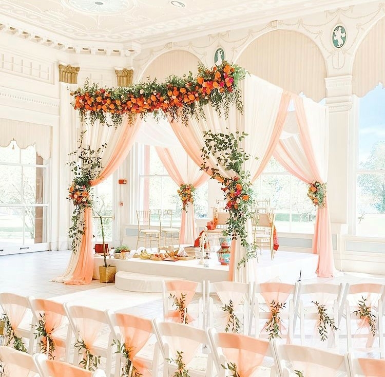 Peach and white wedding mandap decorated with flowers.